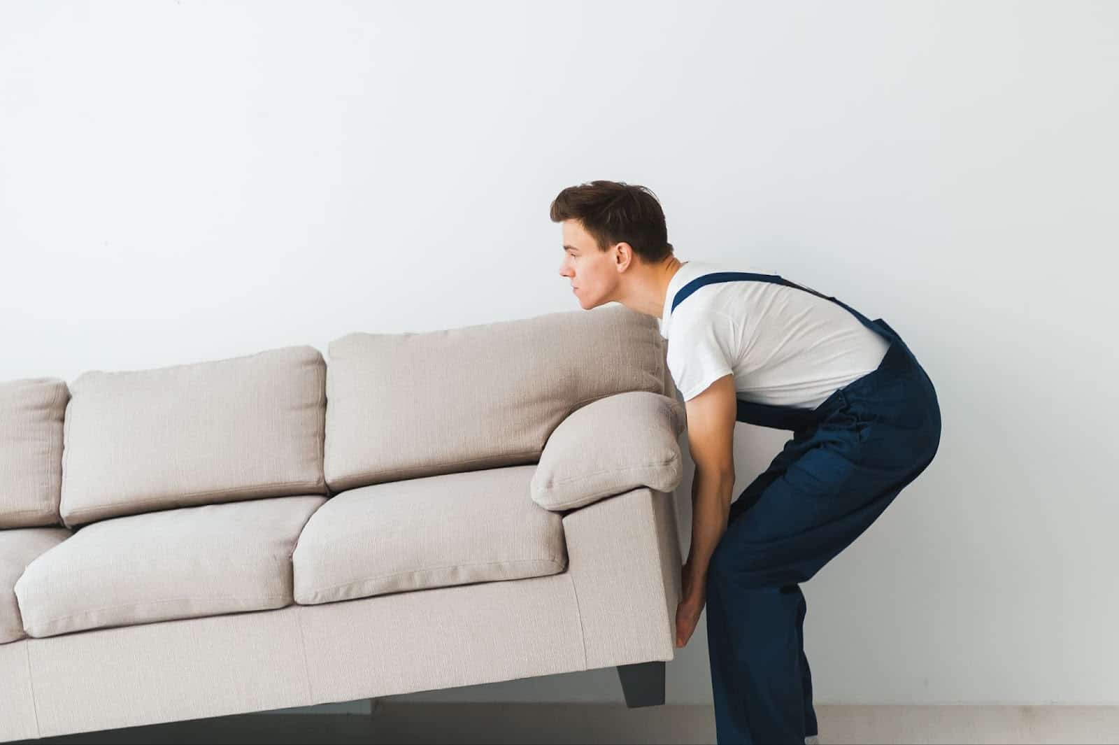 Flyttearbeider løfter en beige sofa innendørs